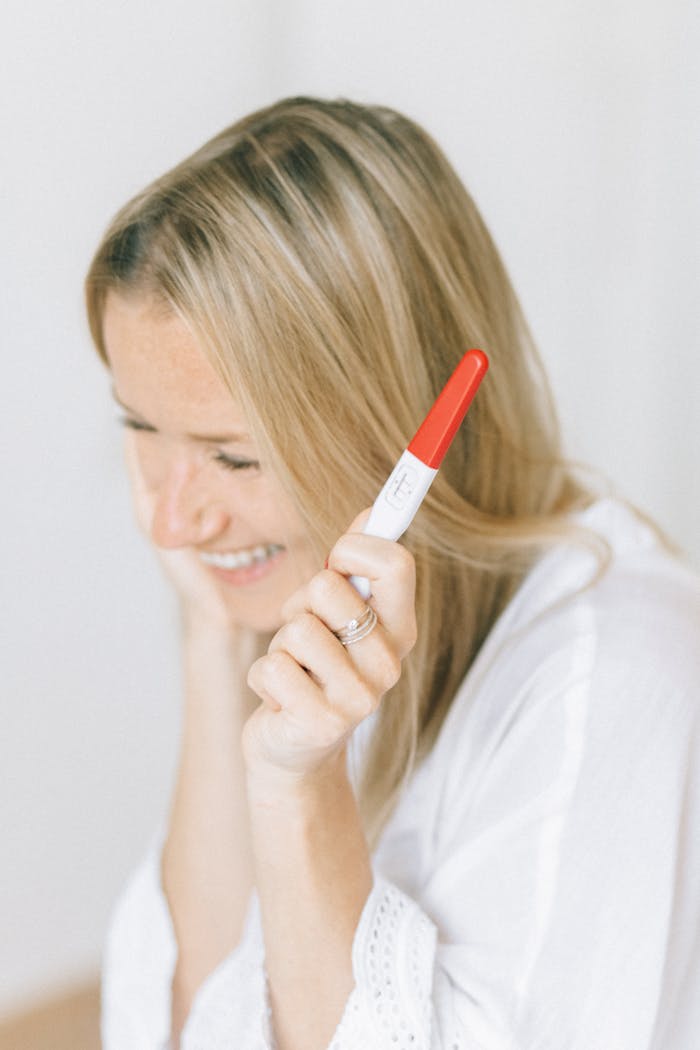 Joyful woman smiling while holding a positive pregnancy test, expressing excitement.