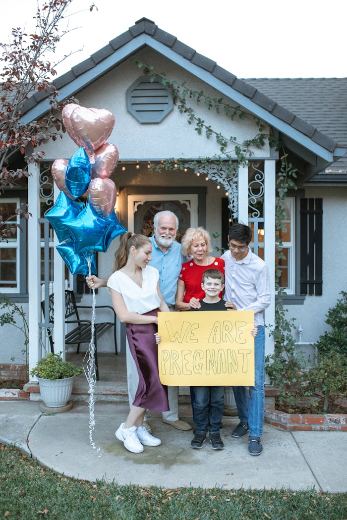 A family joyfully announces a pregnancy with a sign and balloons outside their home.