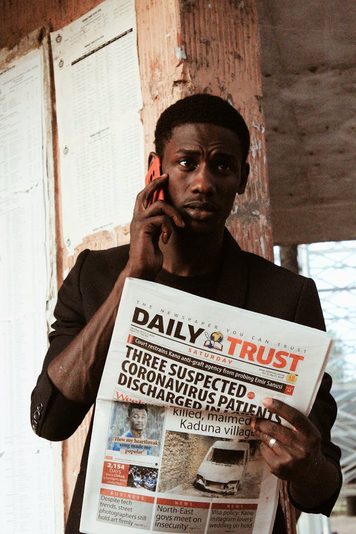 Man holding newspaper with COVID-19 headline, talking on phone outdoors.